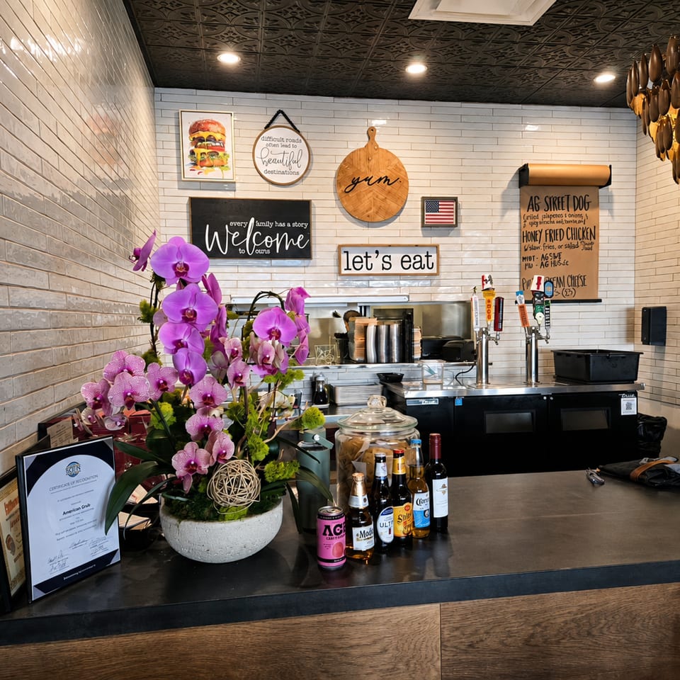Restaurant counter with purple orchids, drinks, and menu boards on a white subway tile wall.